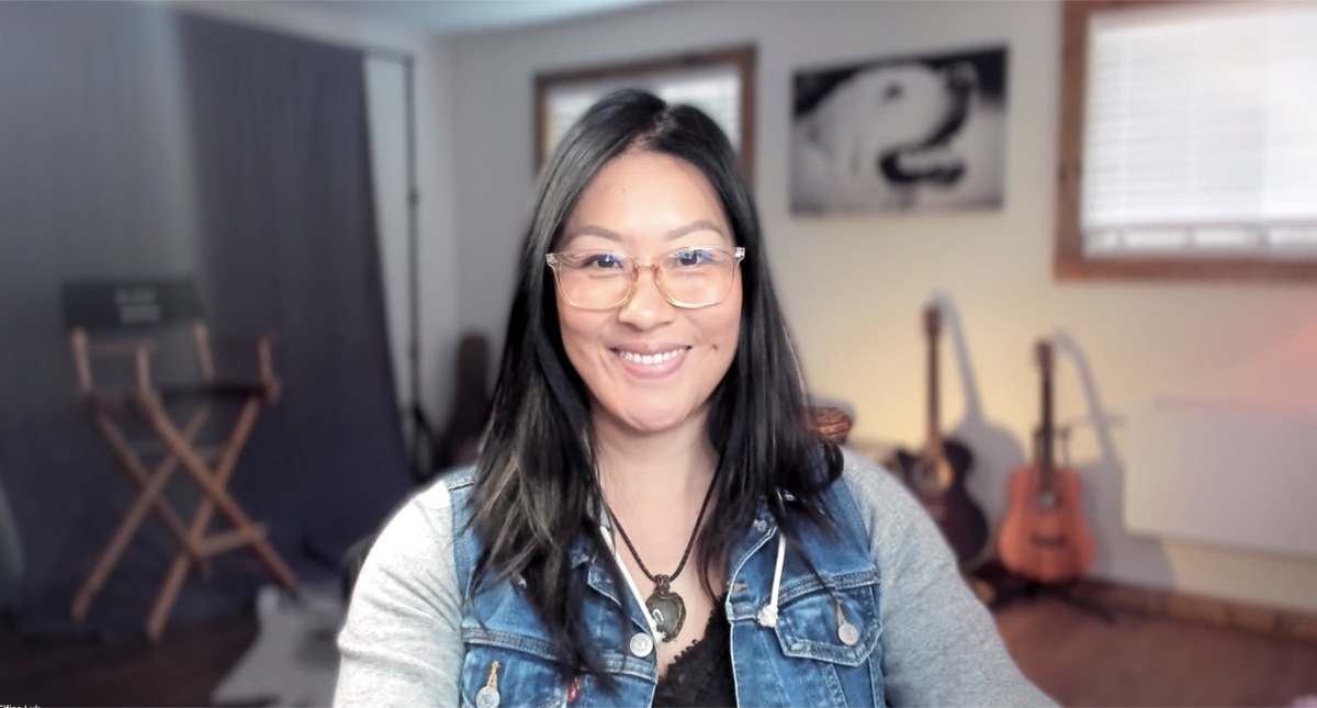 Elfina in her actual home filming setup — director's chair in the background, warm natural light on her face, real space
